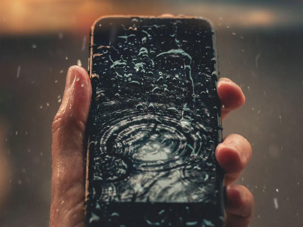 Kézben tartott telefon, a kijelzőn esőcseppek